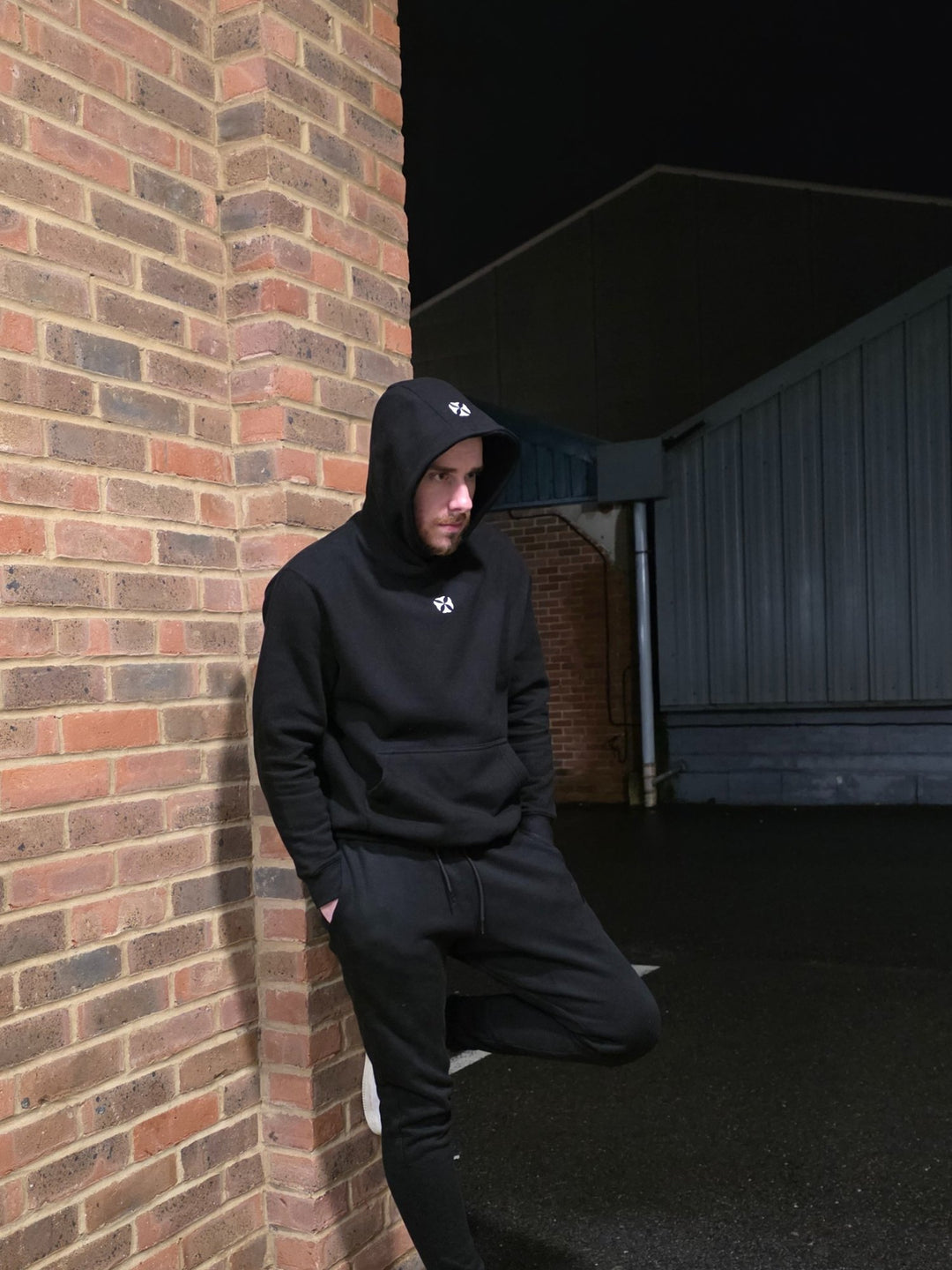 A man in a black LCKY INC hoodie stands against a wall